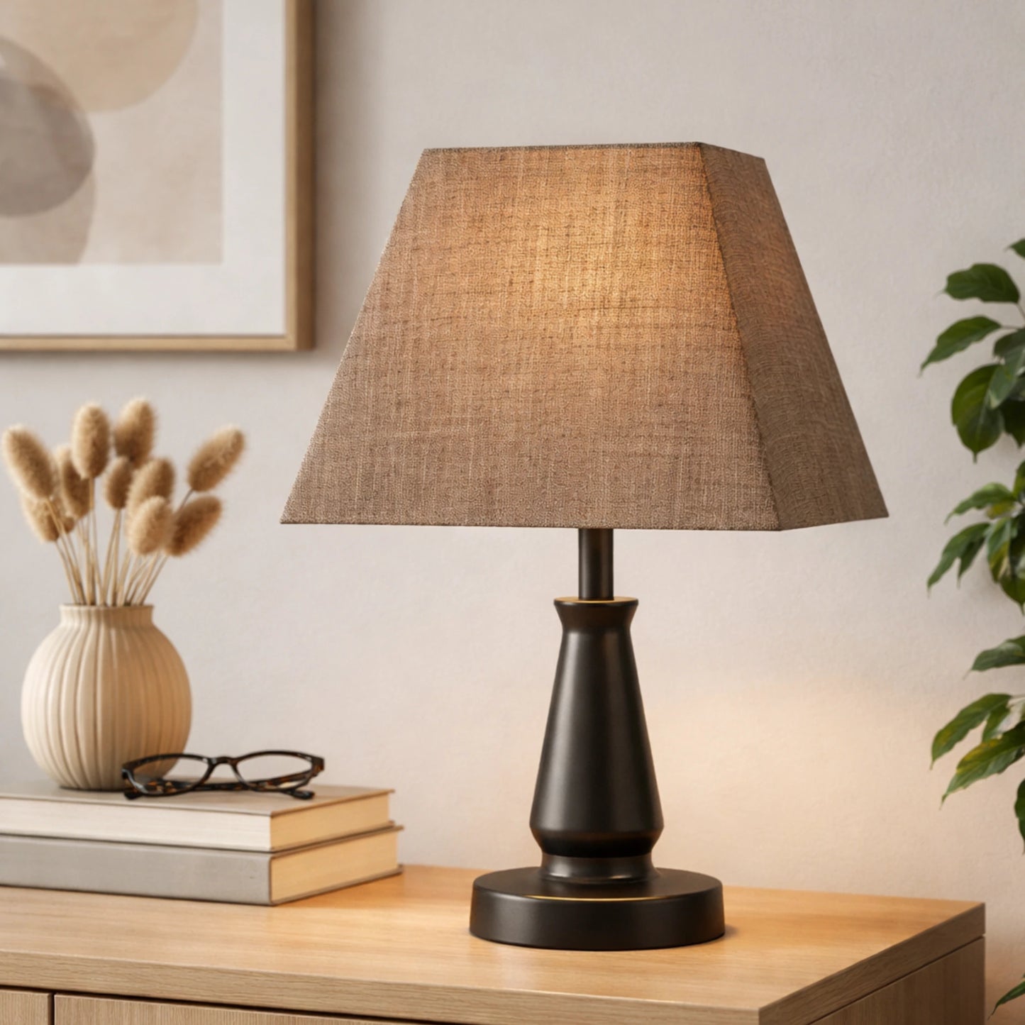 Wohnbeispiel: quadratischer brauner Lampenschirm aus Stoff auf einer schwarzen Tischlampe, platziert auf einem Holztisch mit Trockenblumen und Büchern; der Schirm strahlt warmes, diffuses Licht aus und erzeugt eine gemütliche Atmosphäre,Artikelnummer 30425-636.