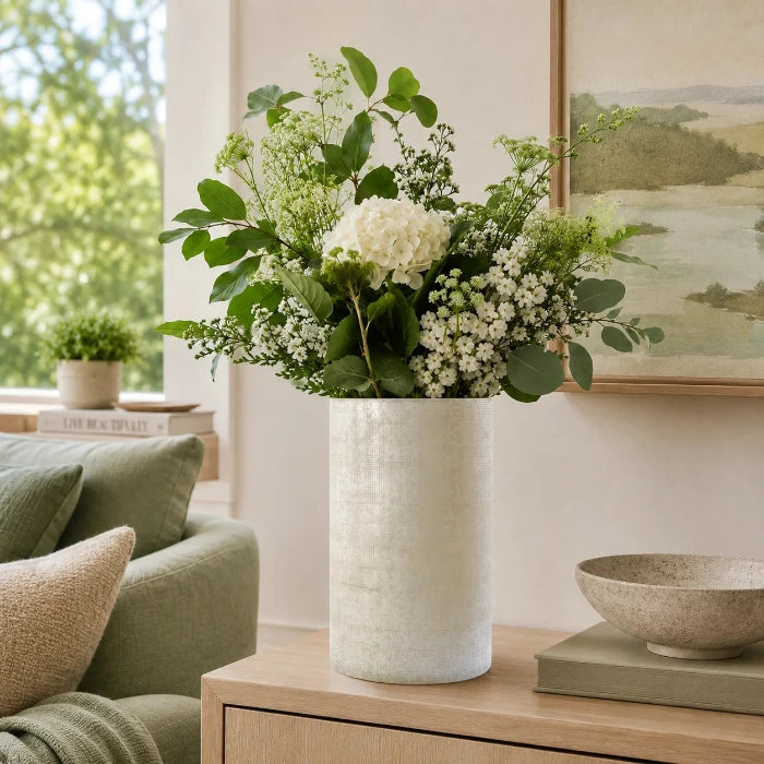 Beige strukturierte Glasvase mit frischem weiß-grünem Blumenstrauß auf einem Sideboard in einem modernen Wohnzimmer.