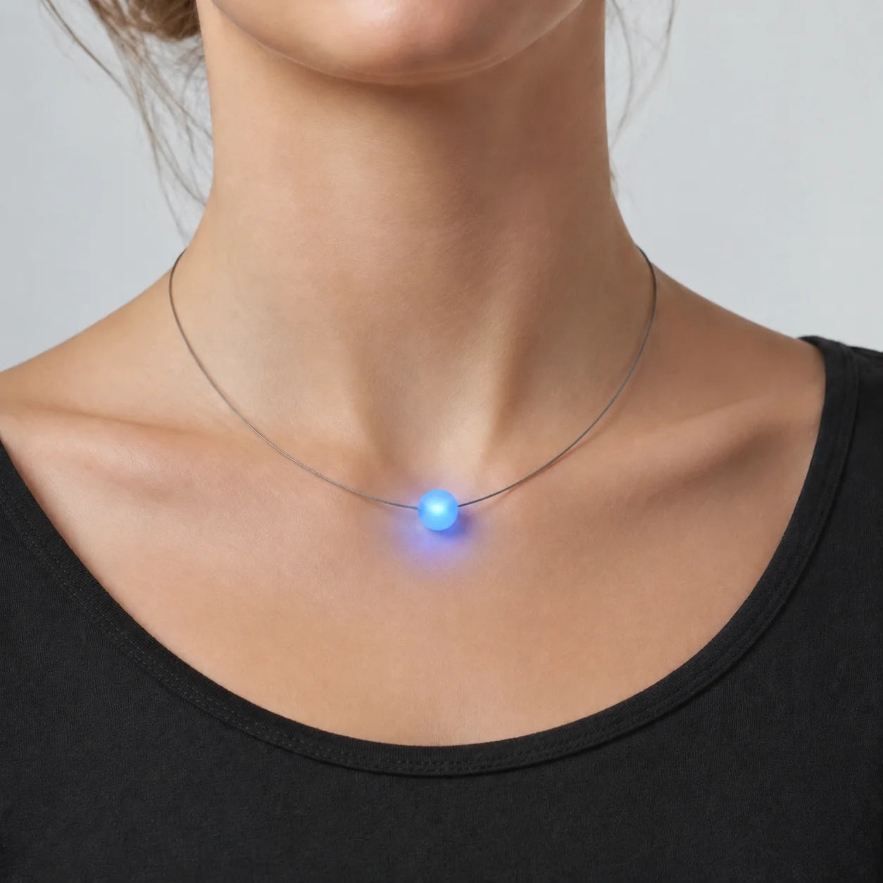 Junge Frau trägt eine blau leuchtende Firejewel LED-Halskette mit kleiner Milchglaskugel oberhalb der Schlüsselbeine