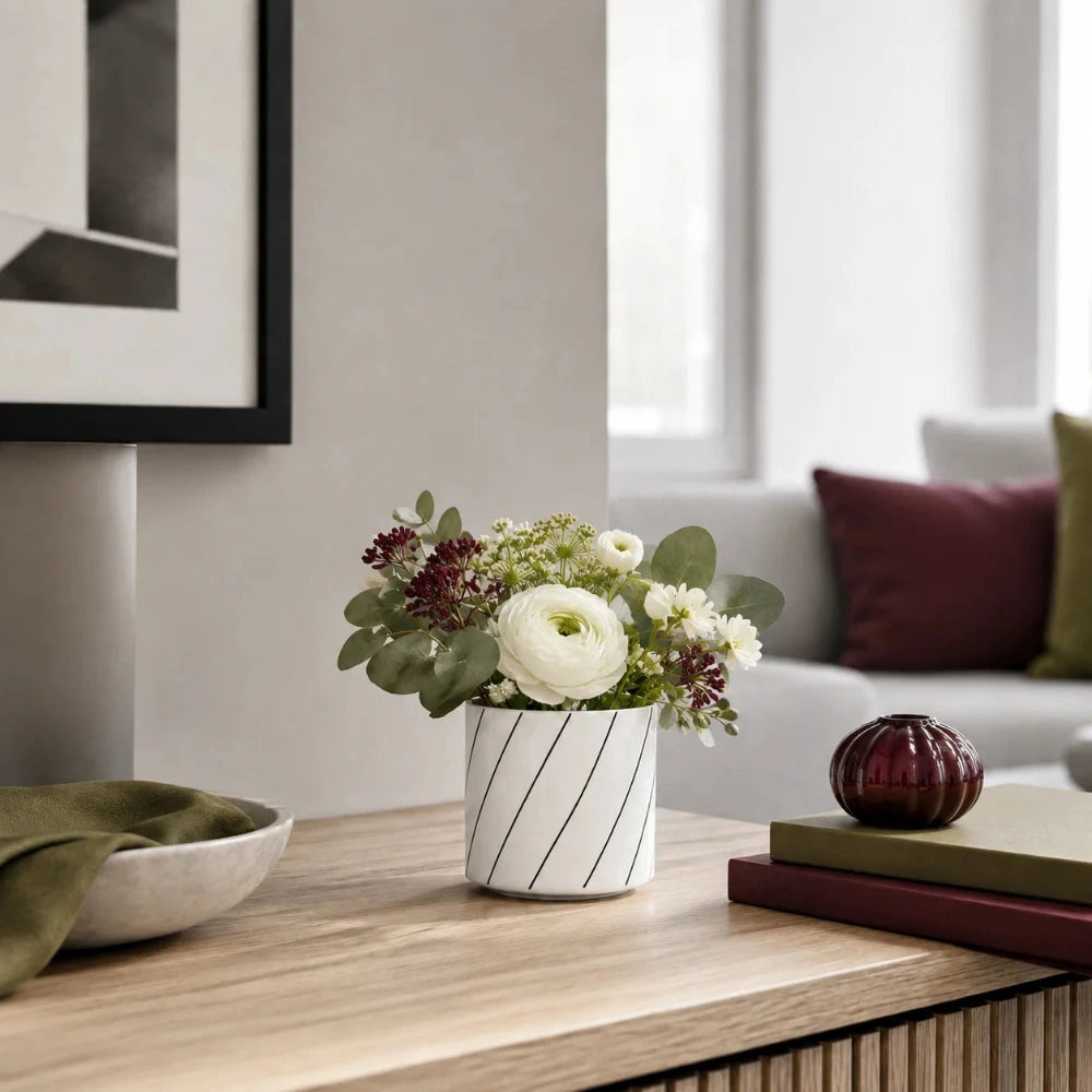 Kleine weiße Porzellan-Mini-Vase mit Blumenstrauß auf einem Sideboard im modernen Wohnzimmer mit Bordeaux- und Olivgrün-Akzenten