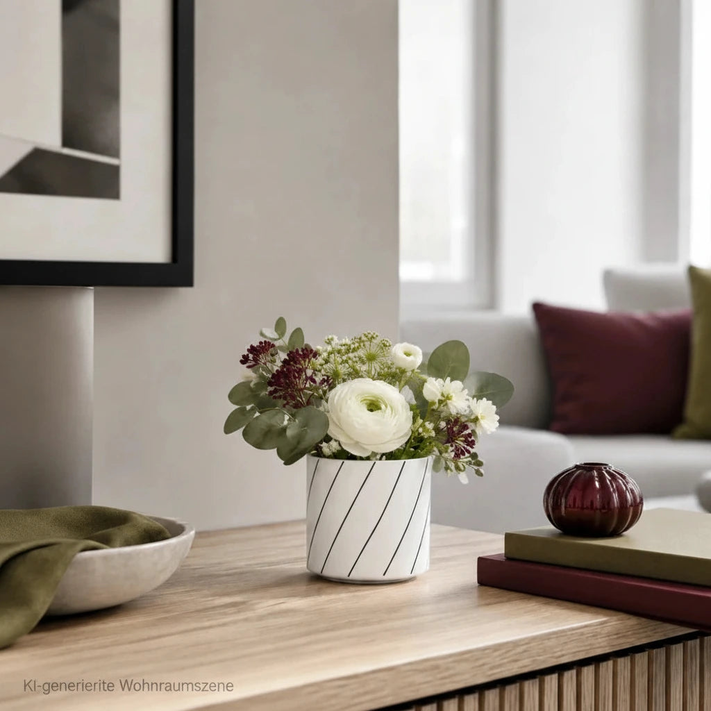 Kleine weiße Porzellan-Mini-Vase mit Blumenstrauß auf einem Sideboard im modernen Wohnzimmer mit Bordeaux- und Olivgrün-Akzenten