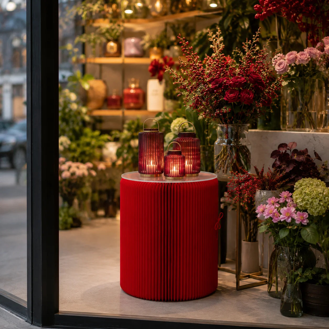 Roter Papur Beistelltisch mit drei dekorativen Laternen im Schaufenster einer modernen Floristik.