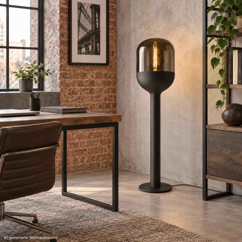 Sompex DOME Stehlampe in Schwarz mit amberfarbenem Glas in einem modernen Arbeitszimmer im Industrial-Stil neben Schreibtisch und Regal.