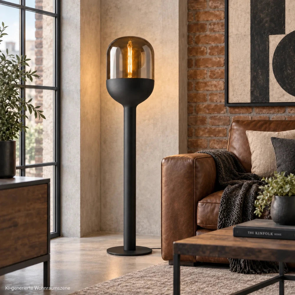 Sompex DOME Stehlampe in Schwarz mit amberfarbenem Glas als Beleuchtung in einem modernen Wohnzimmer im Industrial-Stil neben einem Ledersofa.