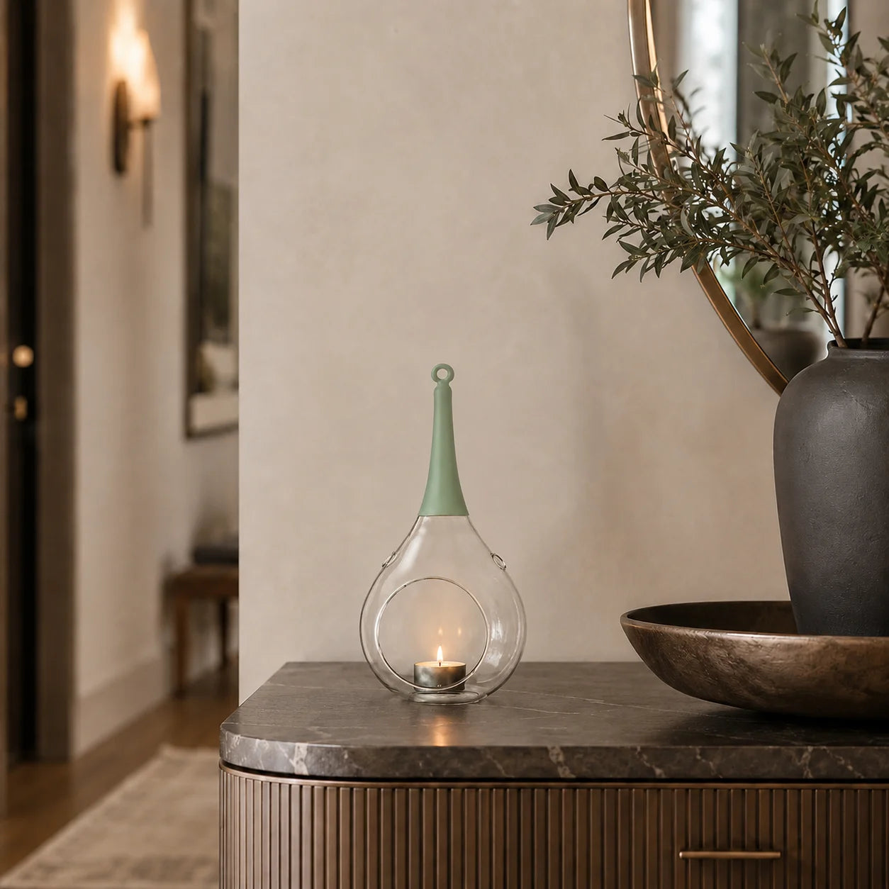 ompex Taura Windlicht in Grün aus Glas mit brennendem Teelicht auf einer modernen Kommode im Flur